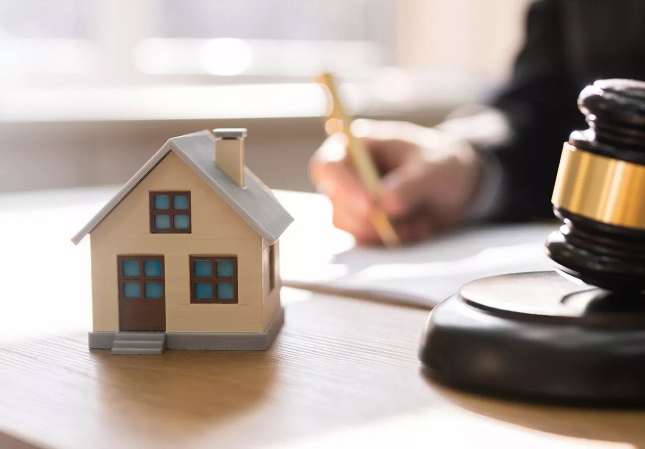 Ein Richterhammer und ein kleines Haus auf einem Tisch.